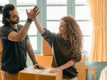 A person organizing their living room, surrounded by neatly packed boxes and items ready for storage. The scene is bright and tidy, reflecting the benefits of spring cleaning and decluttering.